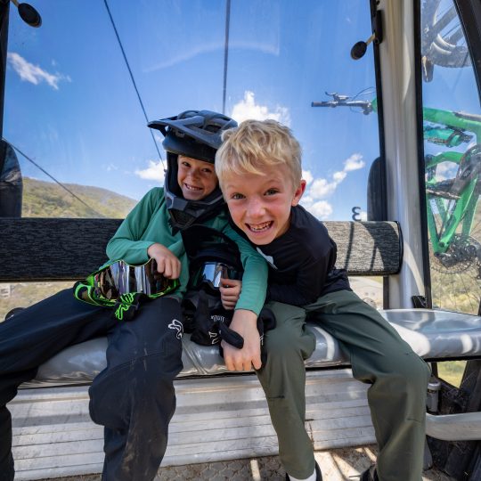 Two children riding up to lift-accessed trails via Merritts Gondola, with their mountain bikes mounted on the outside